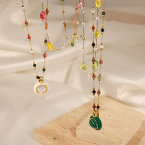 Gemstone cascade layered necklace with colorful beads and charms, including white oval and green malachite pendants.