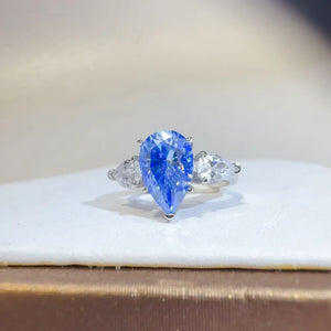 Azure pear cut moissanite trilogy ring in silver with clear accent stones.