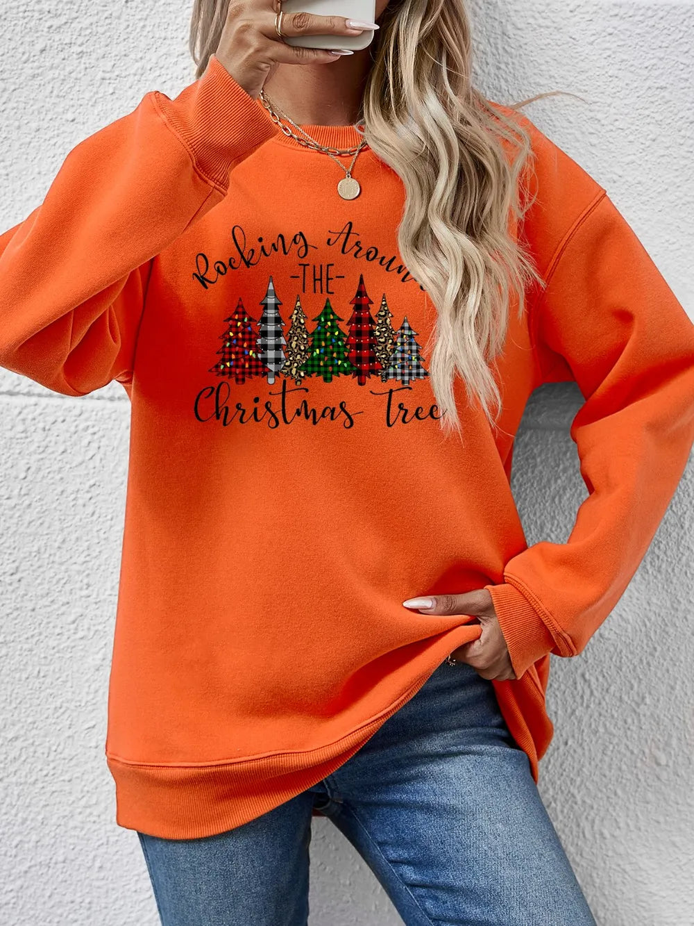 Orange crewneck sweatshirt with graphic Christmas trees and text.