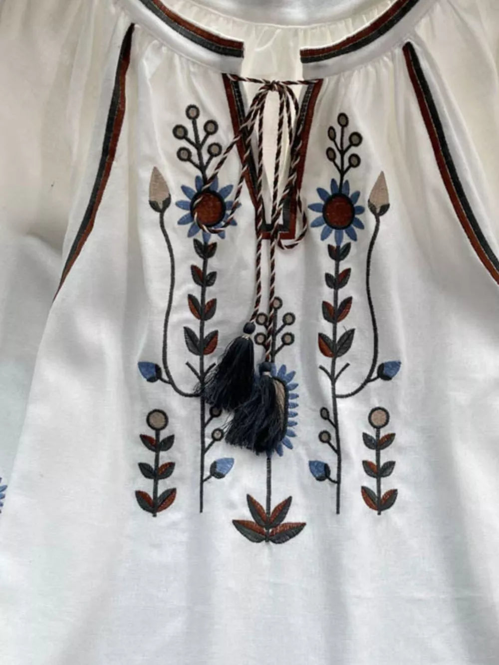 White tie neck blouse with colorful floral embroidery and tassels