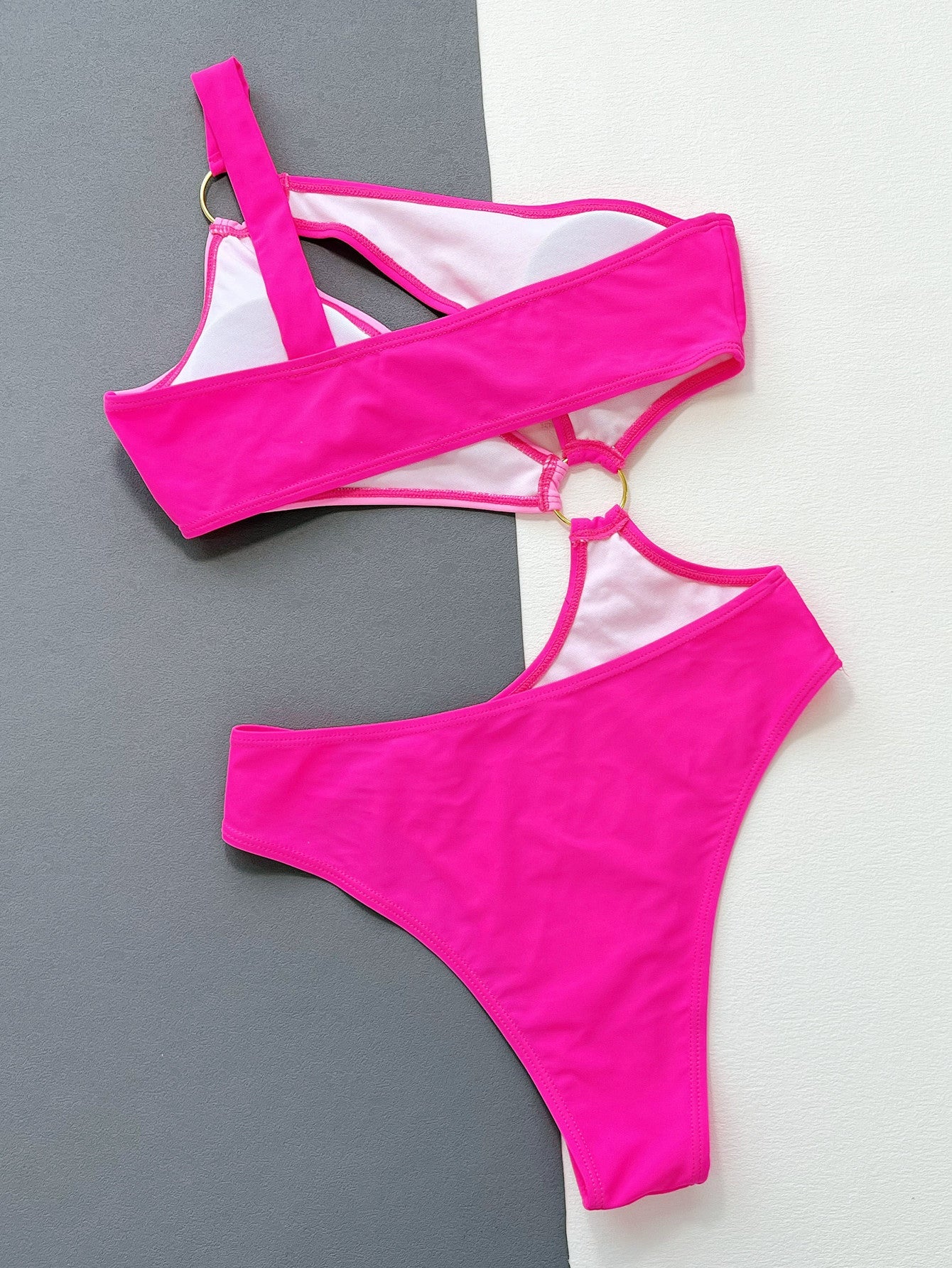Hot pink one-piece swimsuit with asymmetric strap, cut-out detail, and gold ring accents.