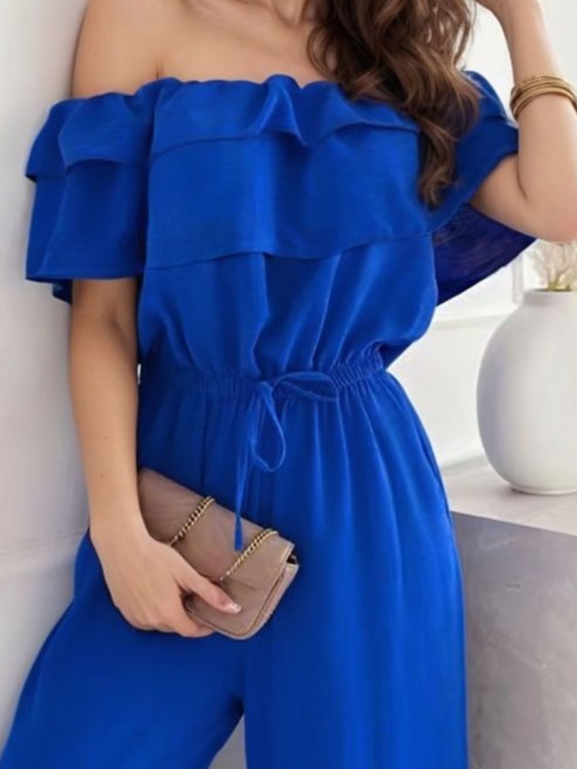Royal blue off-the-shoulder jumpsuit with ruffle detail and drawstring waist.