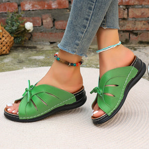 Green criss-cross wedge sandals with bow detail and white stitching.