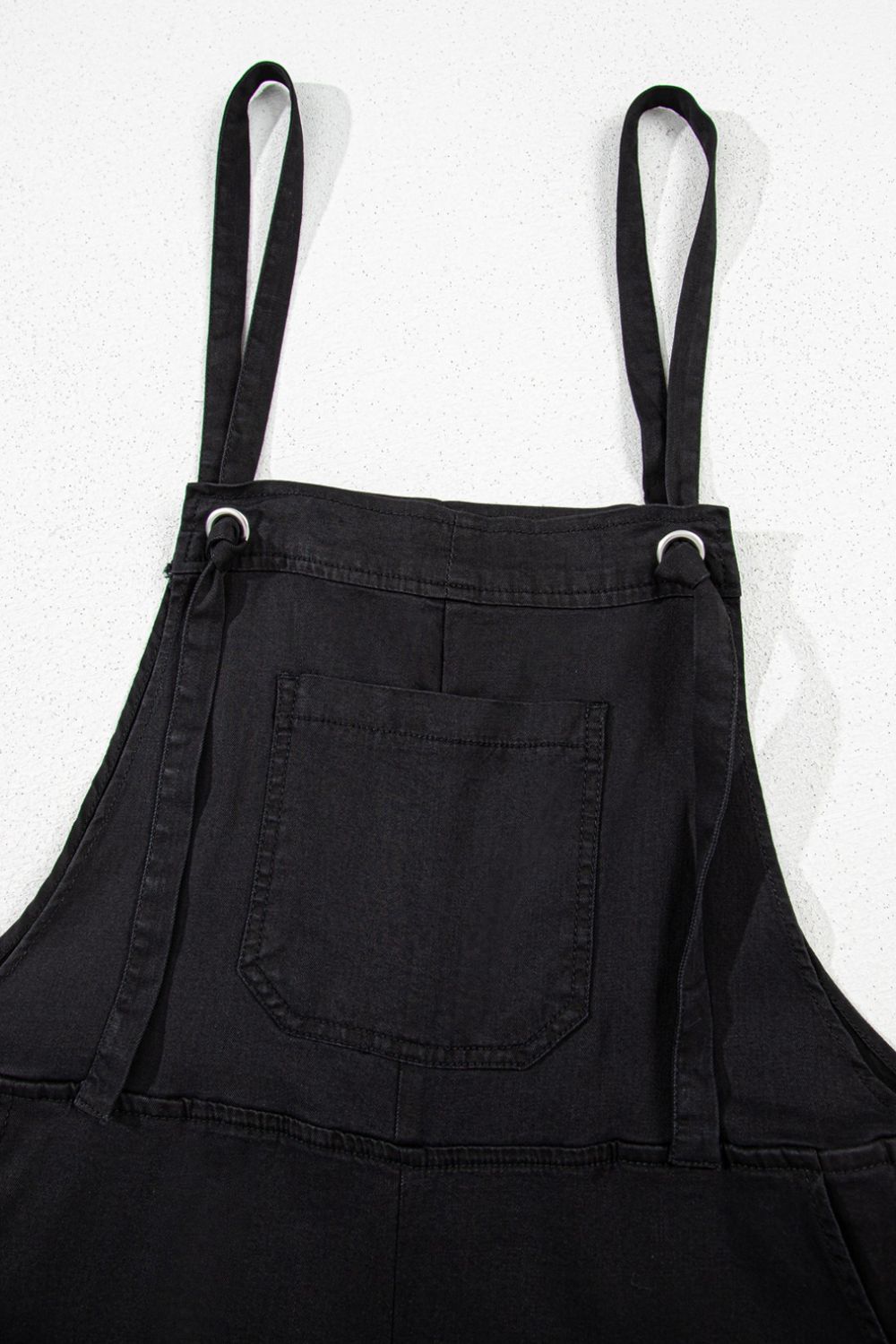 Black denim romper with adjustable straps and a front pocket.