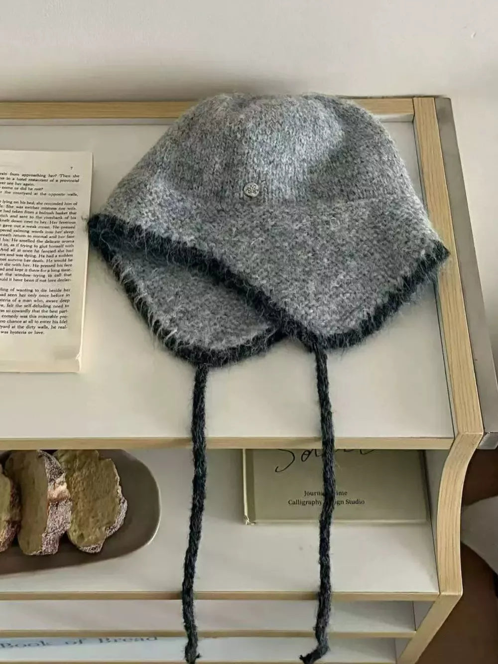 Gray wool-blend hat with ear flaps, braided ties, and dark contrast trim.