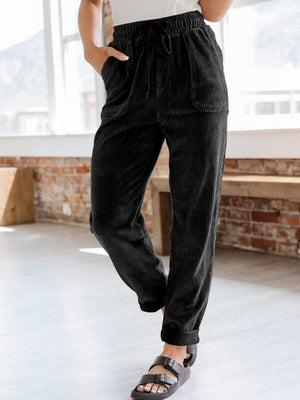 Black corduroy tapered trousers with drawstring waist and pockets.