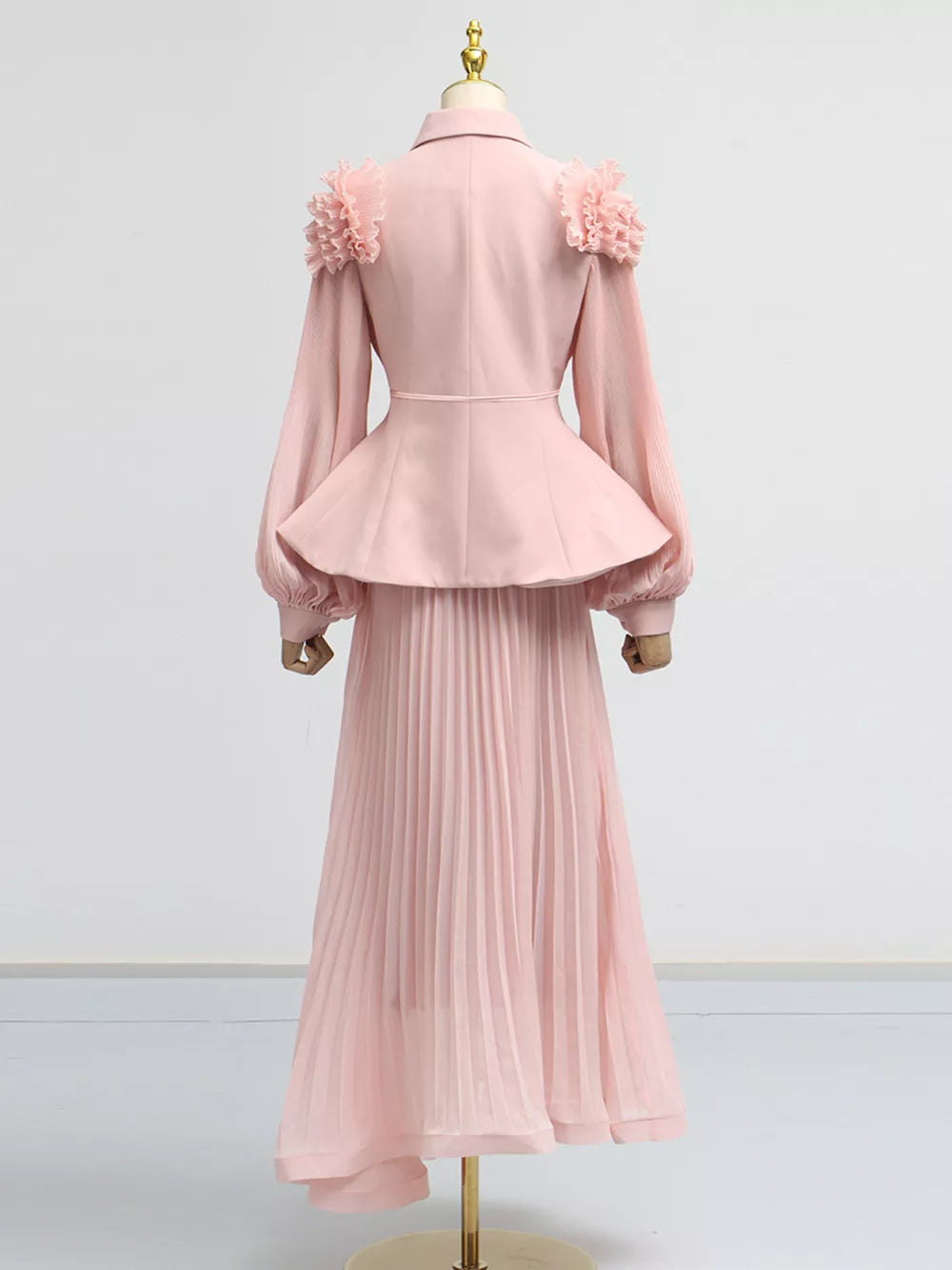 Pink two-piece skirt suit with frill collar, balloon sleeves, peplum jacket, and pleated midi skirt.