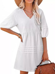 White cotton blend mini dress with puff sleeves, V-neck, and tiered pleated skirt detail.