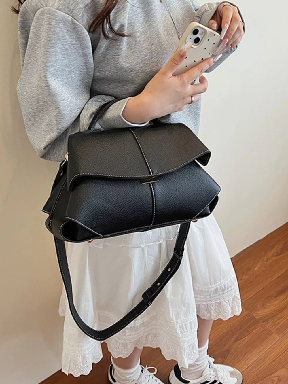 Black textured geometric flap shoulder bag with contrast stitching and adjustable strap.
