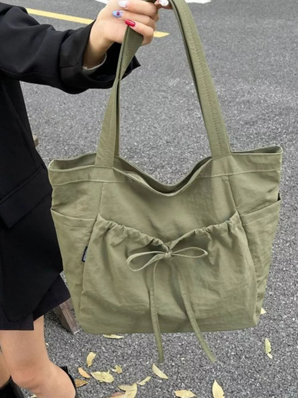 Olive green nylon tote bag with drawstring bow detail and exterior pockets.