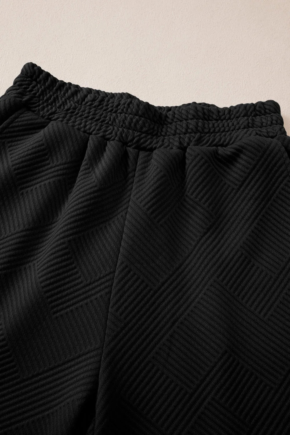 Black quilted knit lounge pants with smocked waistband and geometric pattern detail.