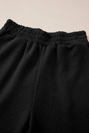 Black quilted knit lounge pants with smocked waistband and geometric pattern detail.