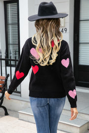 Black crewneck sweater with intarsia hearts in pink and red, long sleeves.