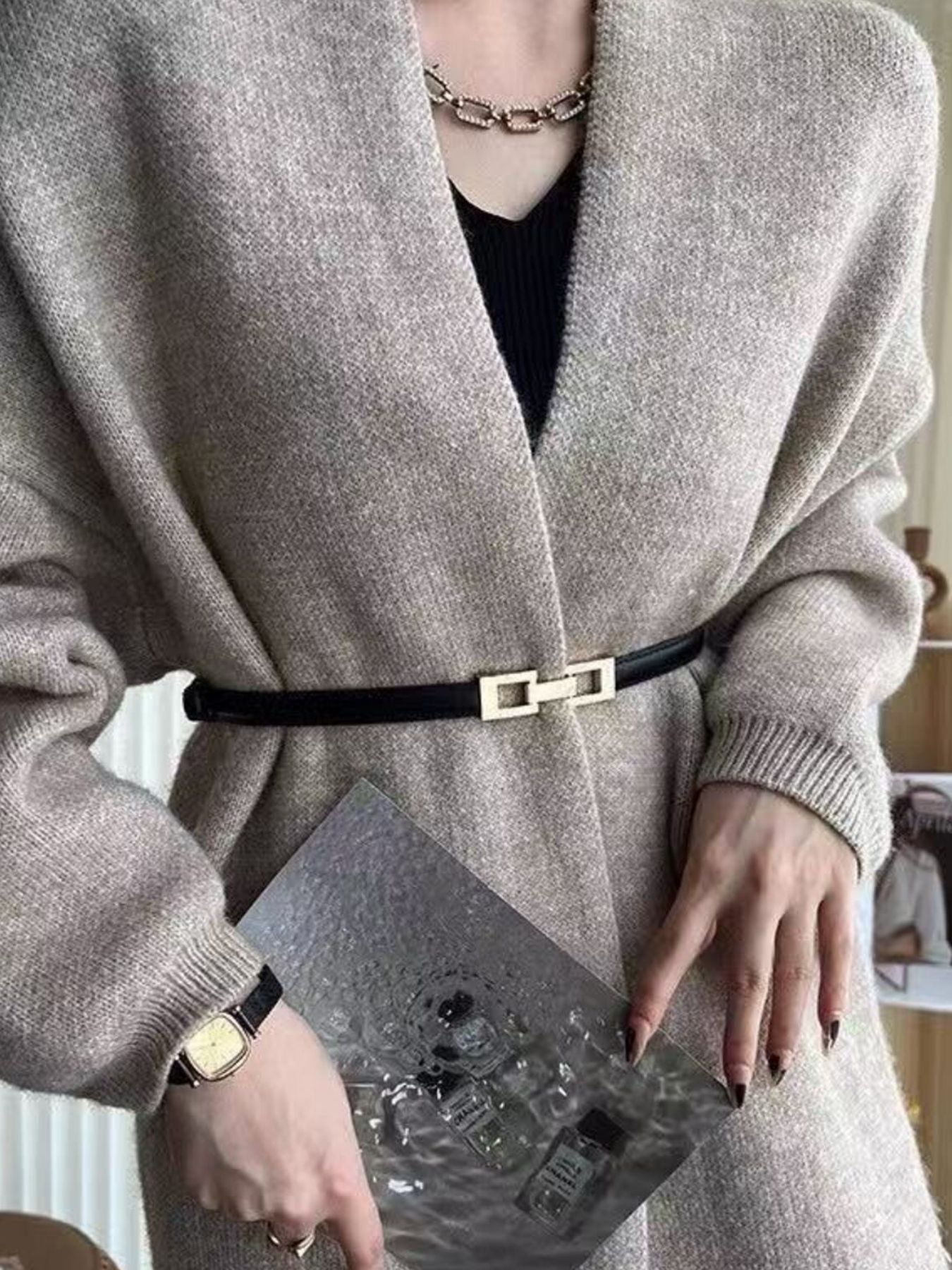 Black cowhide leather belt with gold buckle cinching a cardigan