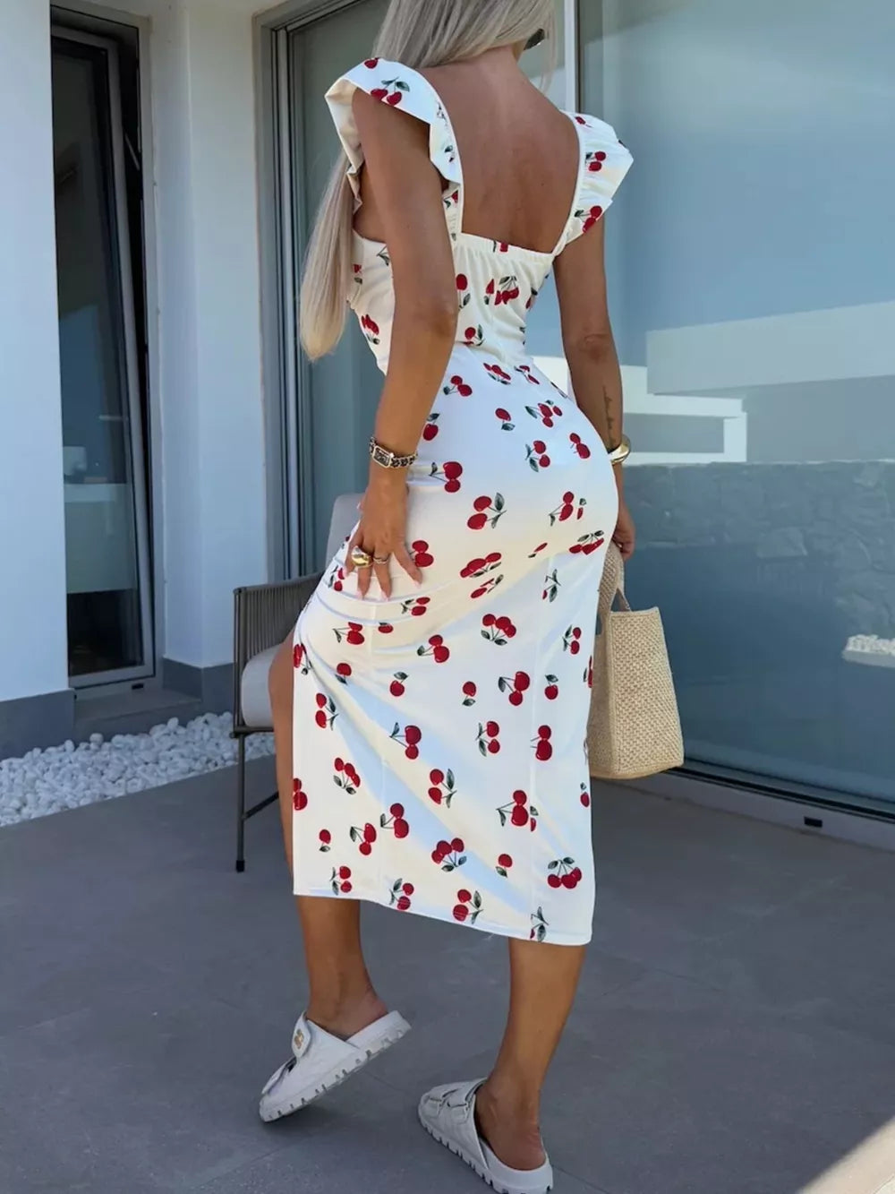White midi dress with cherry print, sweetheart neckline, ruffled cap sleeves, and thigh slit.