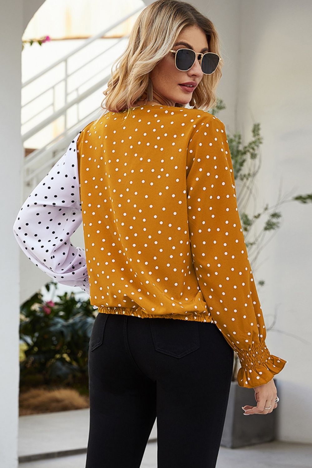 Colorblock polka dot wrap blouse in tangerine with a white polka dot sleeve and ruffled cuff.