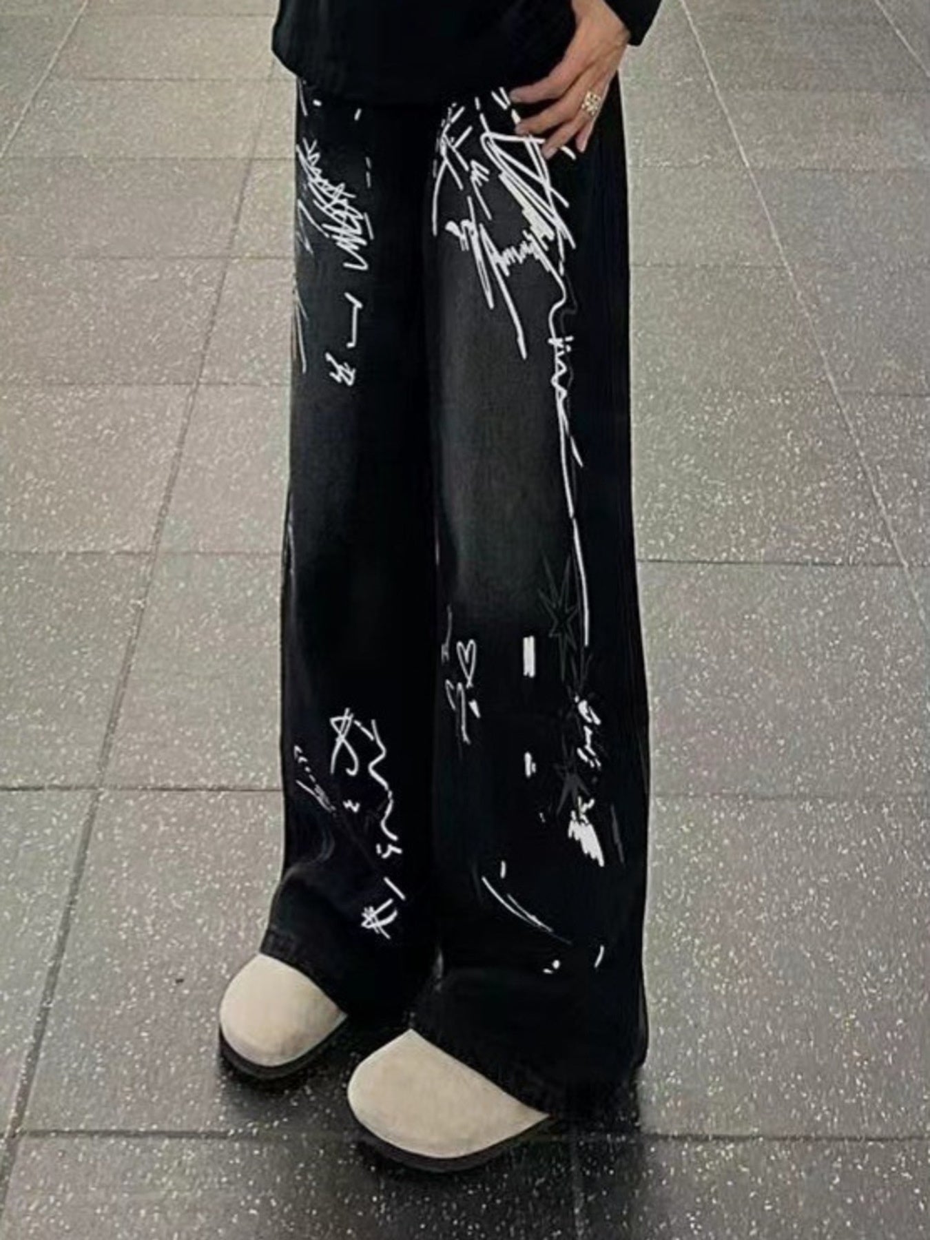 Men's black wide-leg jeans with white graffiti print and light tan shoes.