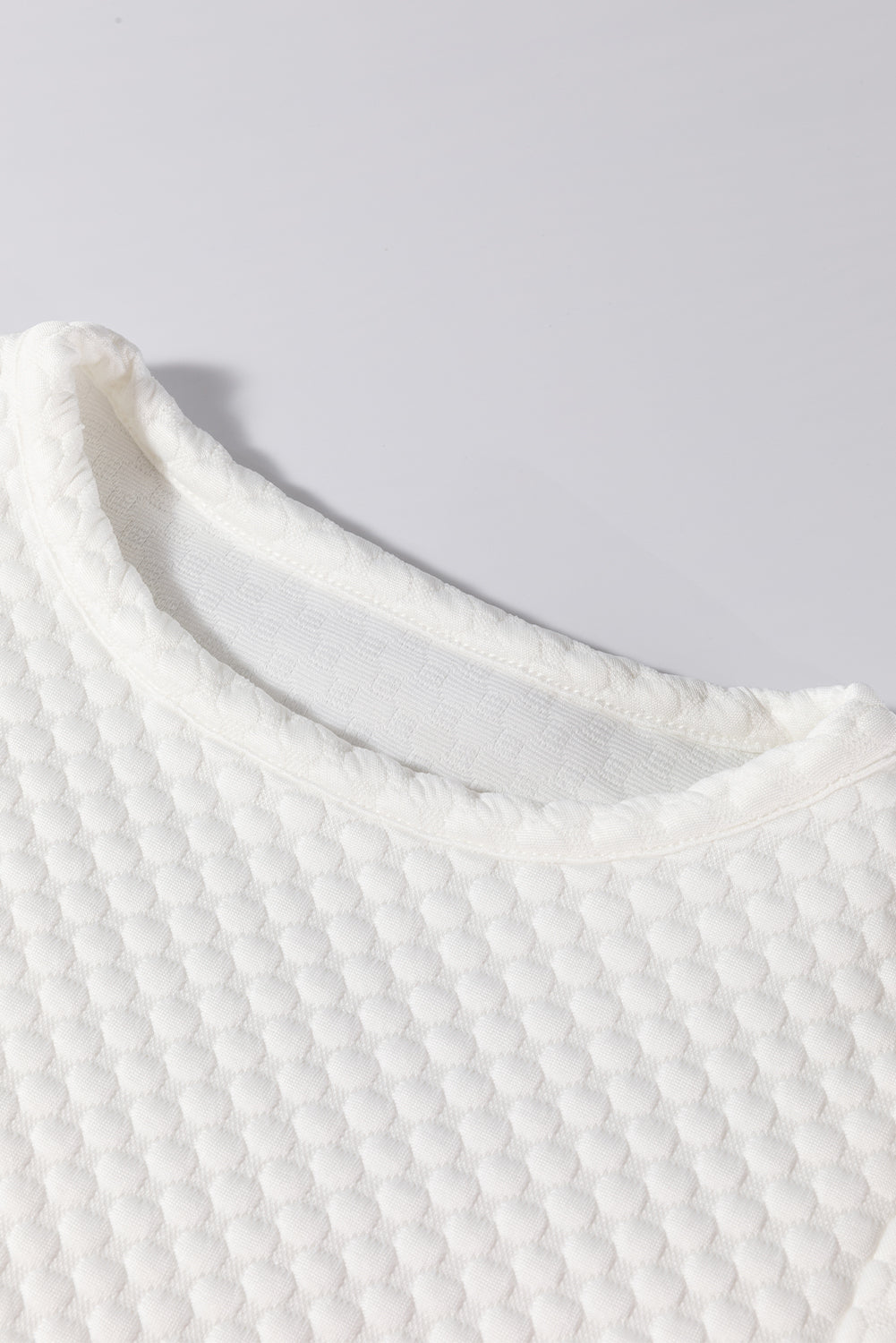 White quilted blouse with a textured diamond pattern and crew neck.