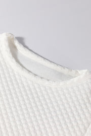 White quilted blouse with a textured diamond pattern and crew neck.