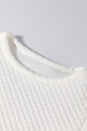 White quilted blouse with a textured diamond pattern and crew neck.