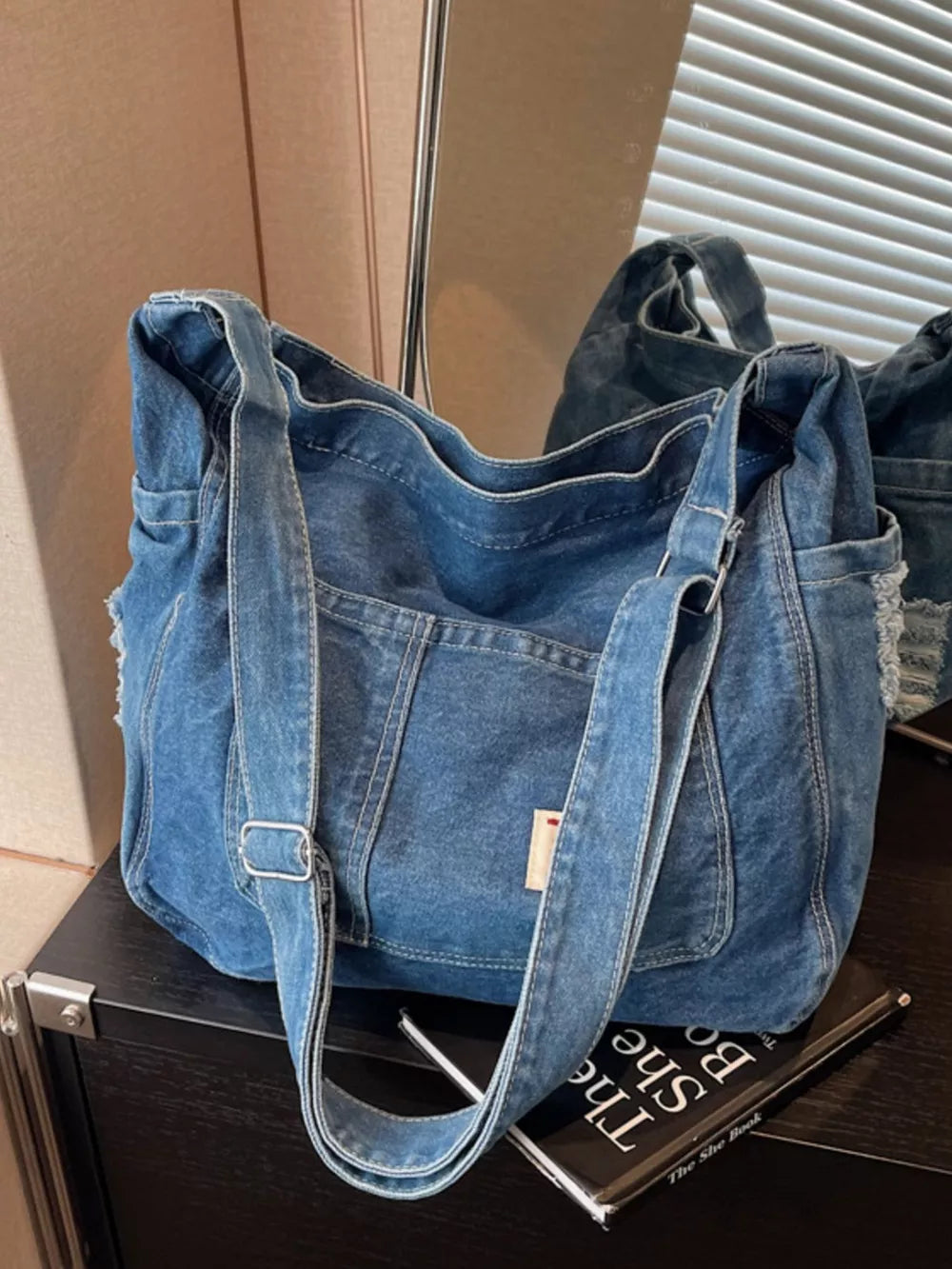 Slouchy blue denim crossbody bag with contrast stitching and adjustable strap.