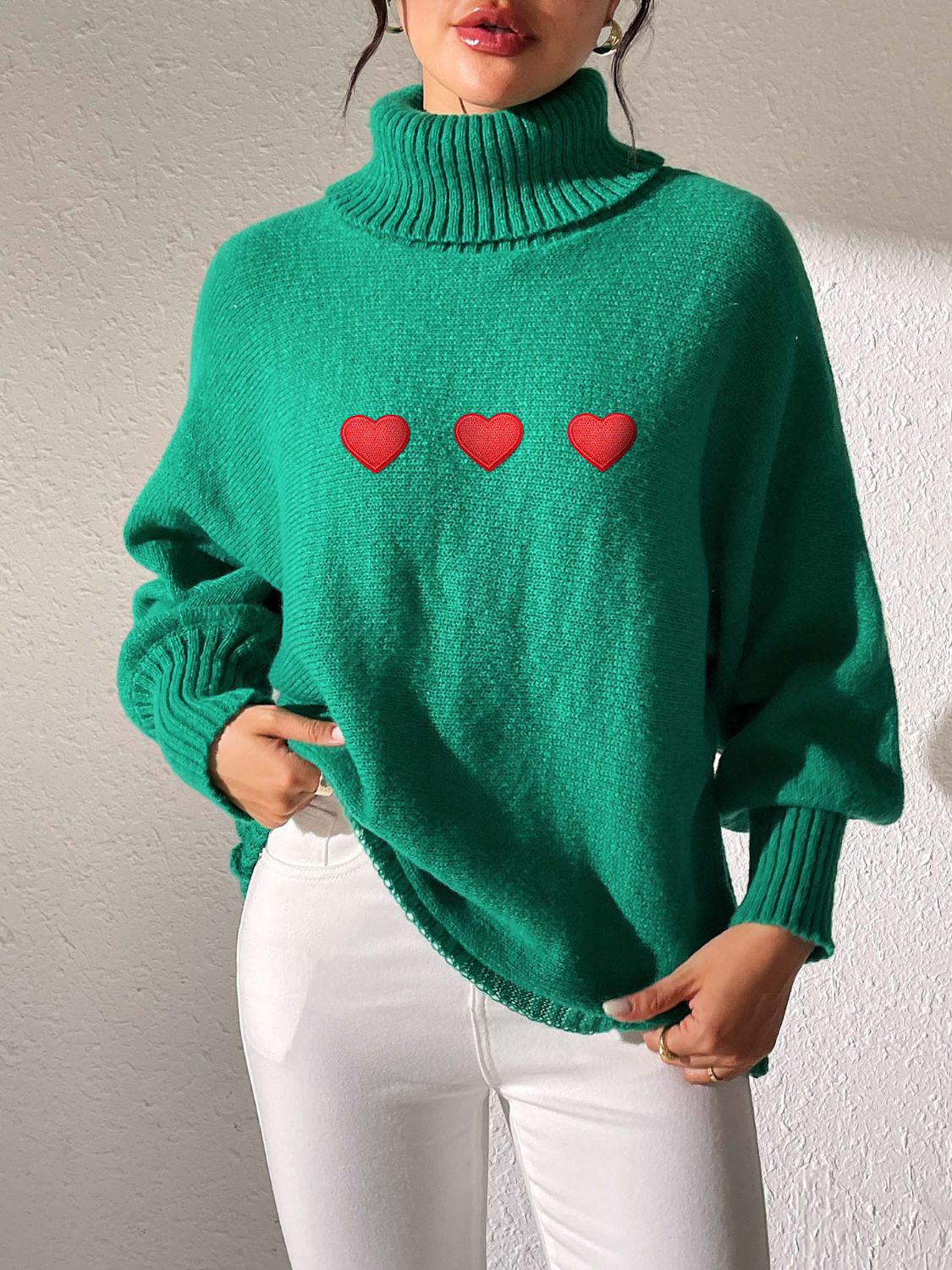 Green turtleneck sweater with balloon sleeves and three red heart appliqués.