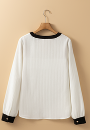 White textured blouse with black trim at neckline and cuffs, long sleeves.