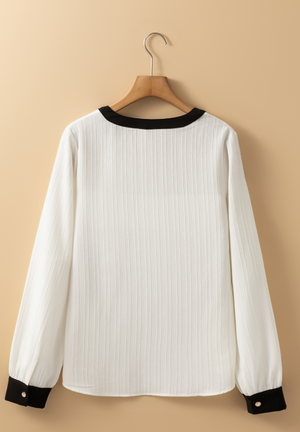 White textured blouse with black trim at neckline and cuffs, long sleeves.