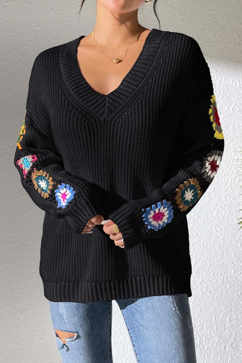 Black knit sweater with colorful granny square sleeve details, V-neck, and ribbed cuffs.