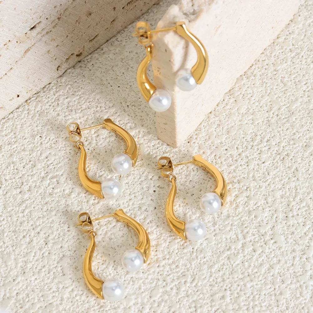 Gold sculptural pearl drop hoop earrings with a modern design.