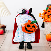 Doll with white sequin dress, red cape, and holding a felt pumpkin.