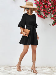 Black tiered sleeve mini dress with tie waist, styled with a straw hat and clutch.