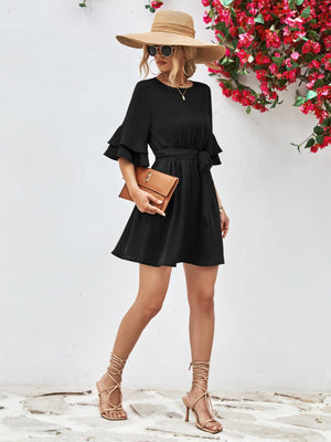 Black tiered sleeve mini dress with tie waist, styled with a straw hat and clutch.