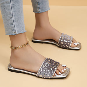 Sequined open-toe slide sandals in silver with a square toe and a gold chain anklet.
