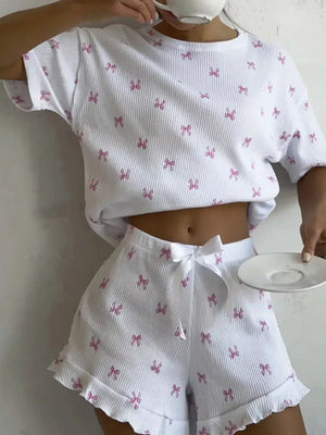 White knit lounge set with pink bow print, cropped t-shirt and ruffled shorts with drawstring.