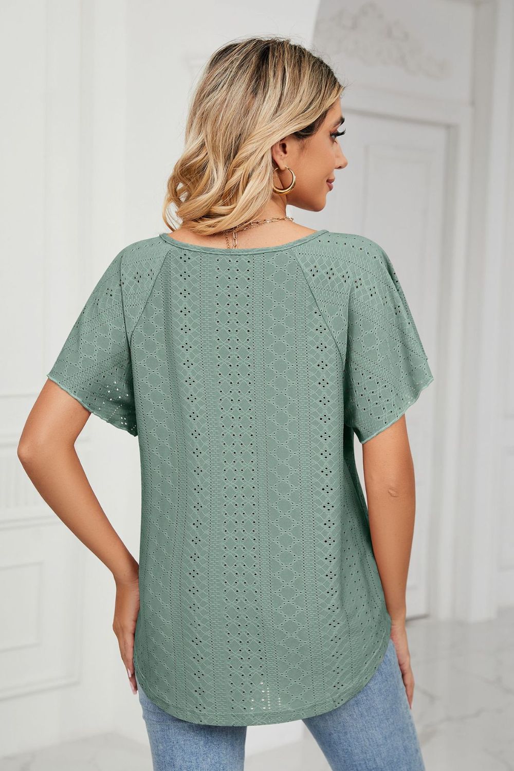 Green eyelet tie-neck blouse with flutter sleeves and a rounded hem.