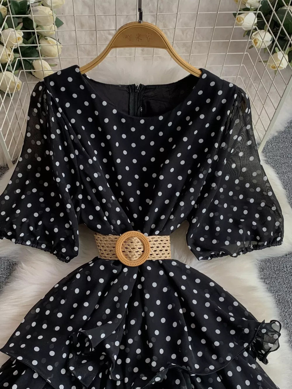Black polka dot tiered dress with puff sleeves and a woven belt.