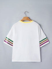 White cotton t-shirt with yellow neckline and sequin striped sleeves in green, gold, and purple.