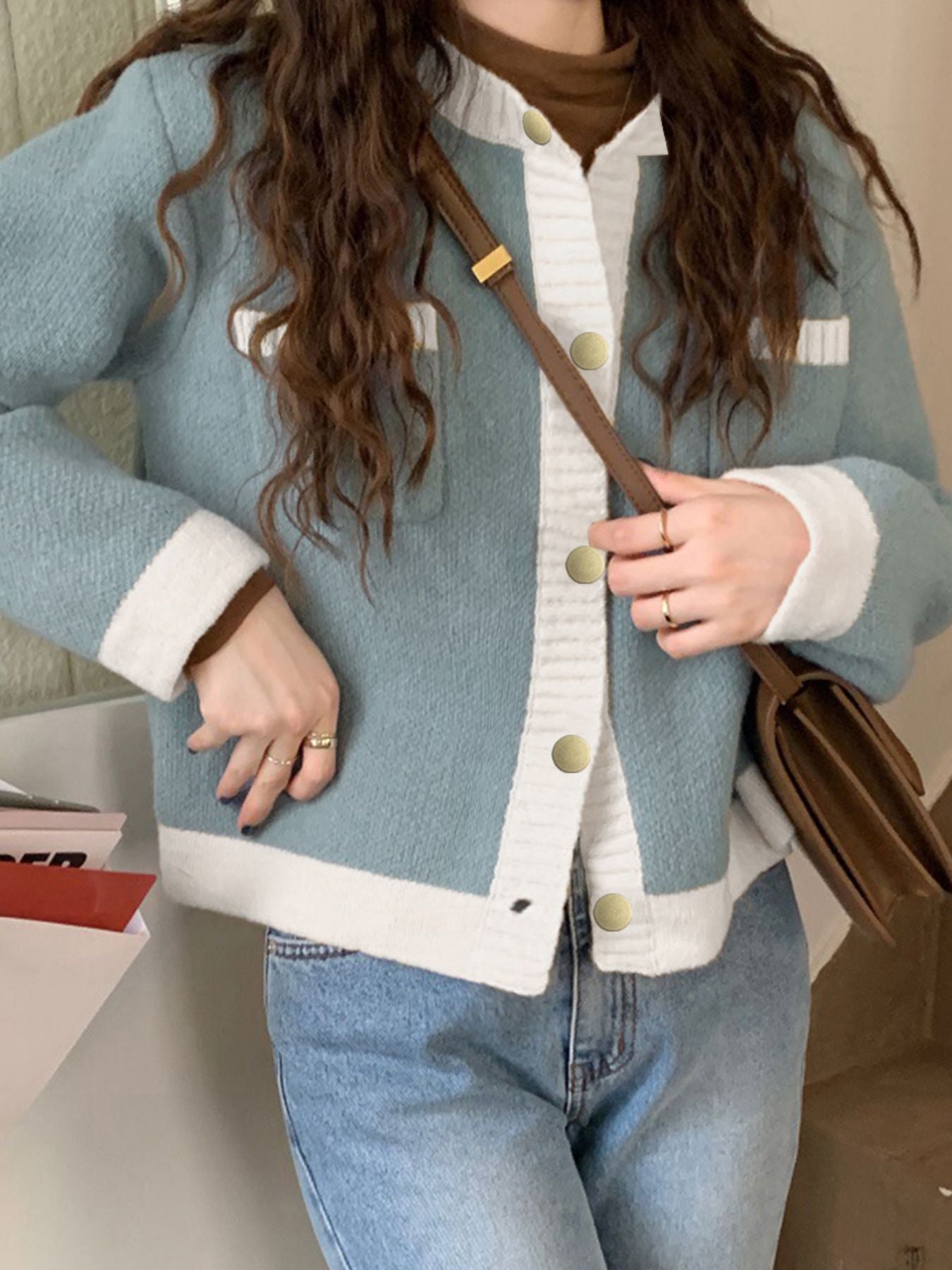 Blue acrylic cardigan with white contrast trim and gold buttons, styled casually.