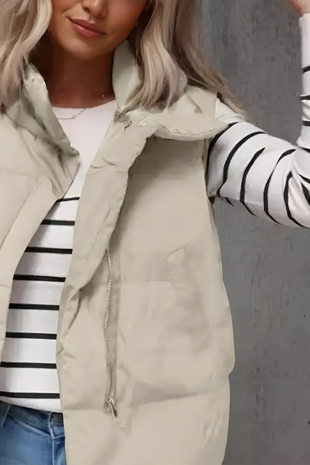 Padded stand collar vest in beige with a silver zipper, worn over a striped long-sleeve shirt.