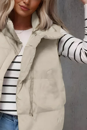 Padded stand collar vest in beige with a silver zipper, worn over a striped long-sleeve shirt.