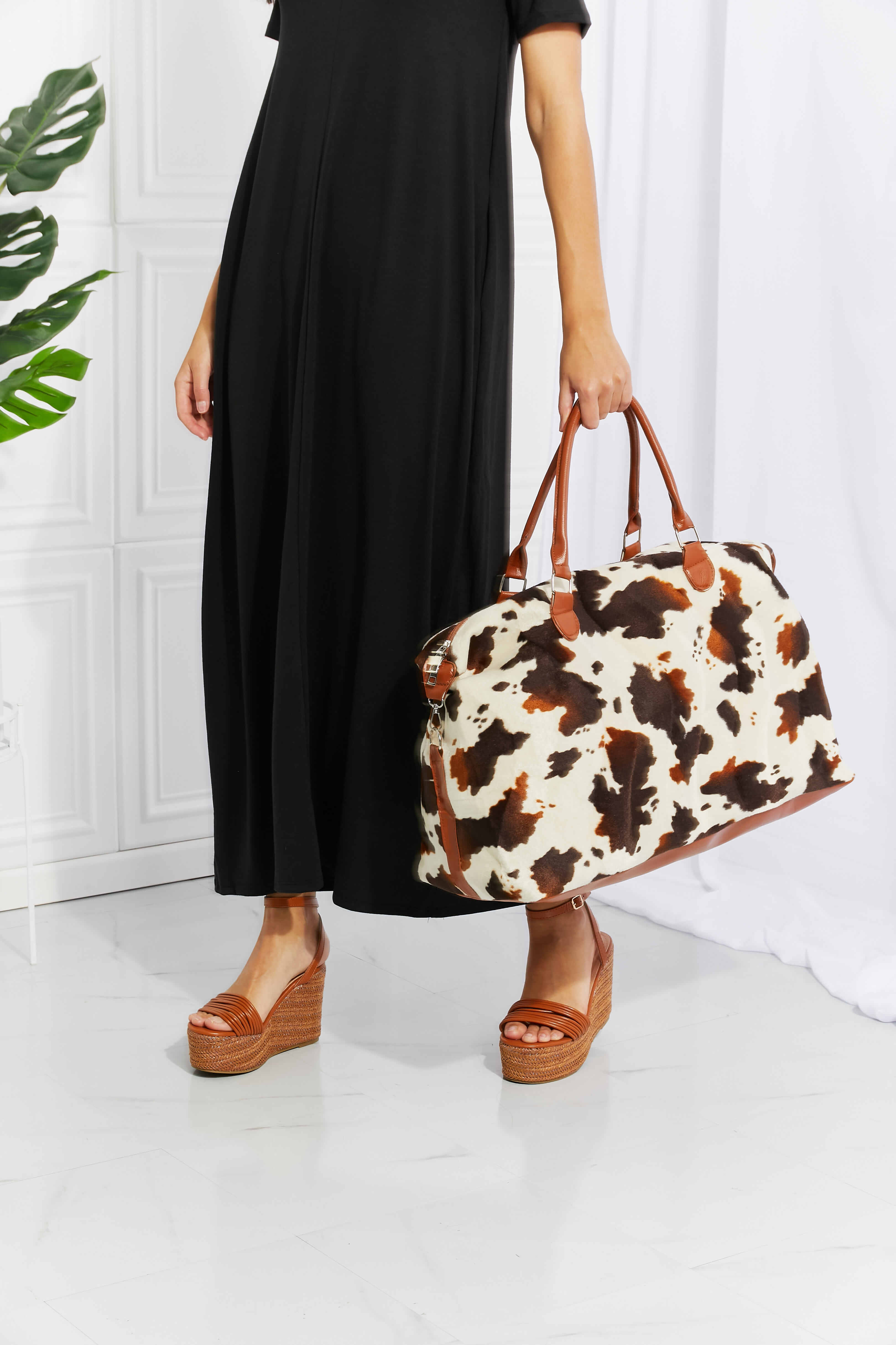 Cowhide print duffel bag with brown leather trim and handles.