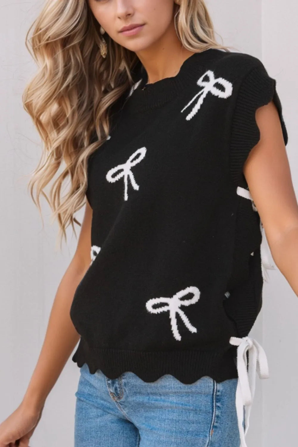 Black knit vest with white bow print, scalloped hem, and tie sides.
