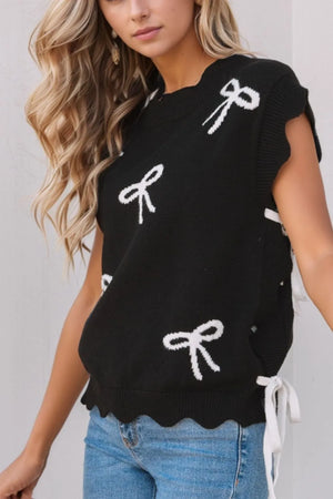 Black knit vest with white bow print, scalloped hem, and tie sides.