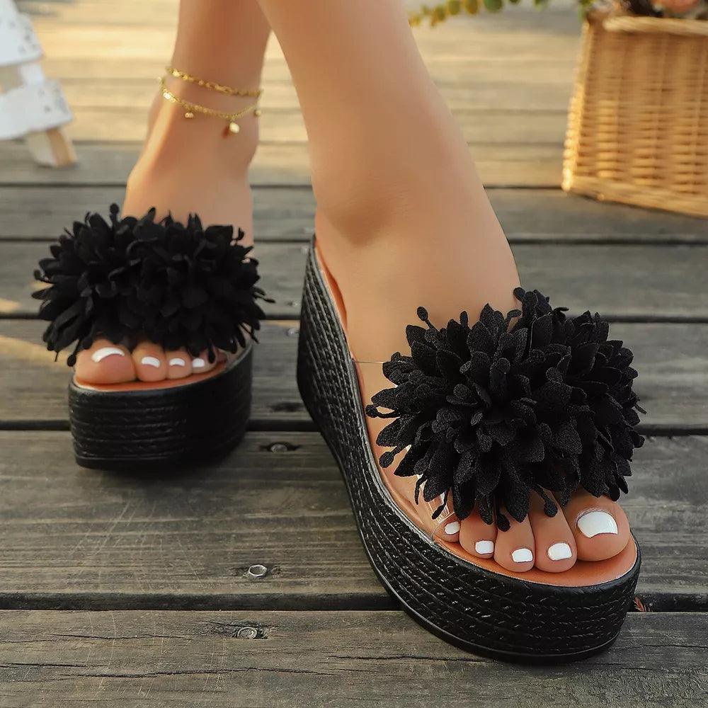 Black wedge sandals with floral pom-pom detail and braided platform.