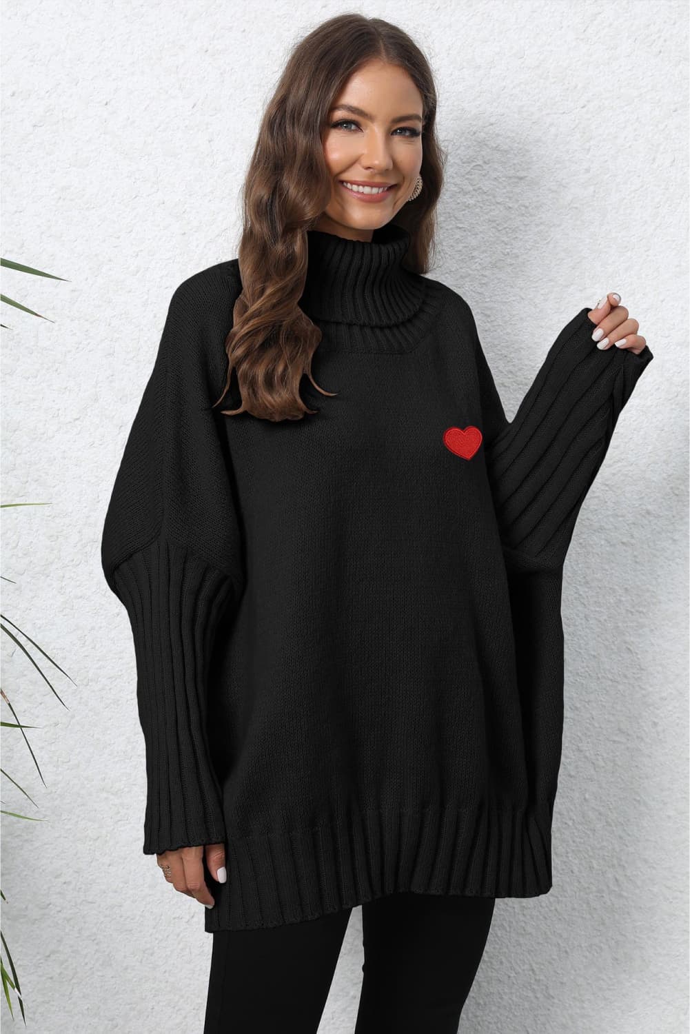 Black batwing knit turtleneck sweater with red heart embroidery and ribbed sleeves.