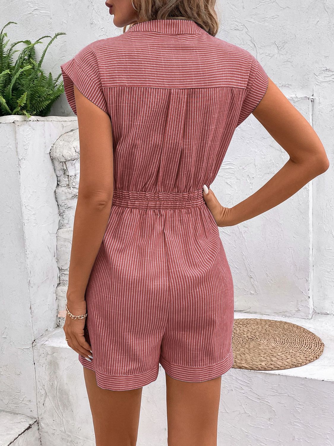 Dusty pink striped shirting romper with short sleeves, collared neckline, and cinched waist tie.