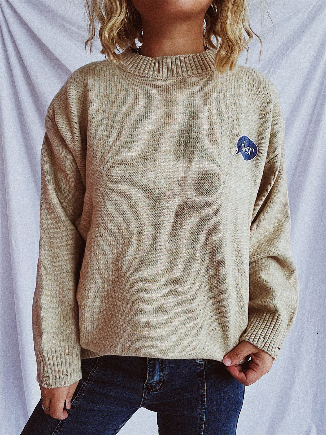 Relaxed knit sweater in dark gray or tan, acrylic, with embroidered character detail.
