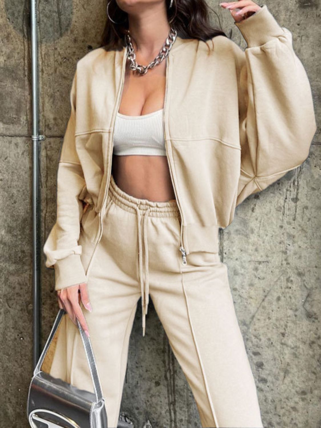 Tan zip-up jacket and drawstring pants set with white crop top and silver bag.