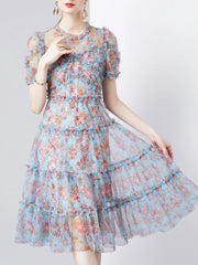 Ruffled floral dress with short sleeves and tiered skirt in light blue with pink and coral flowers.